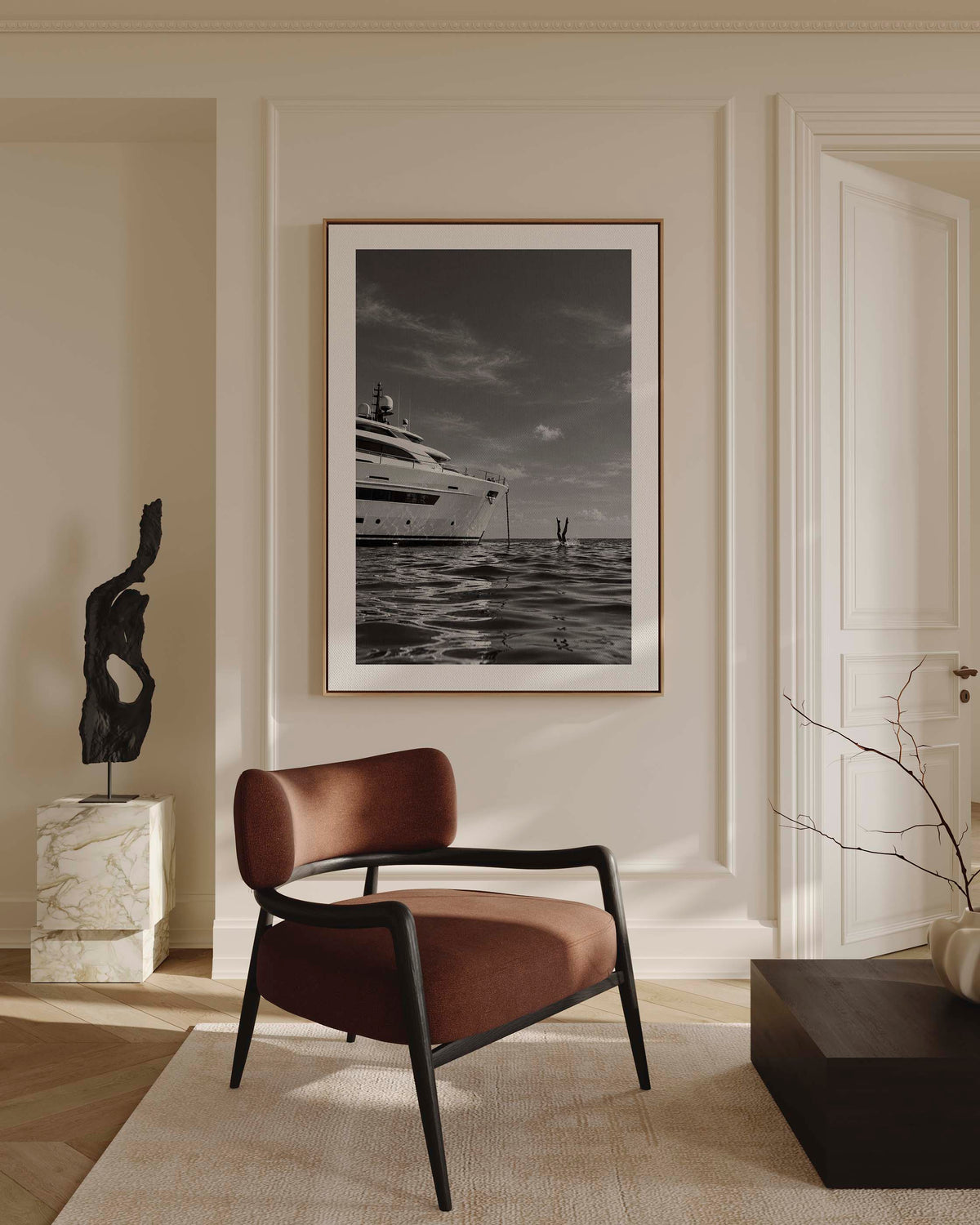 A framed black and white art print of a luxury yacht on the water, styled on a white wall above a bed with white linens and a small wooden stool.