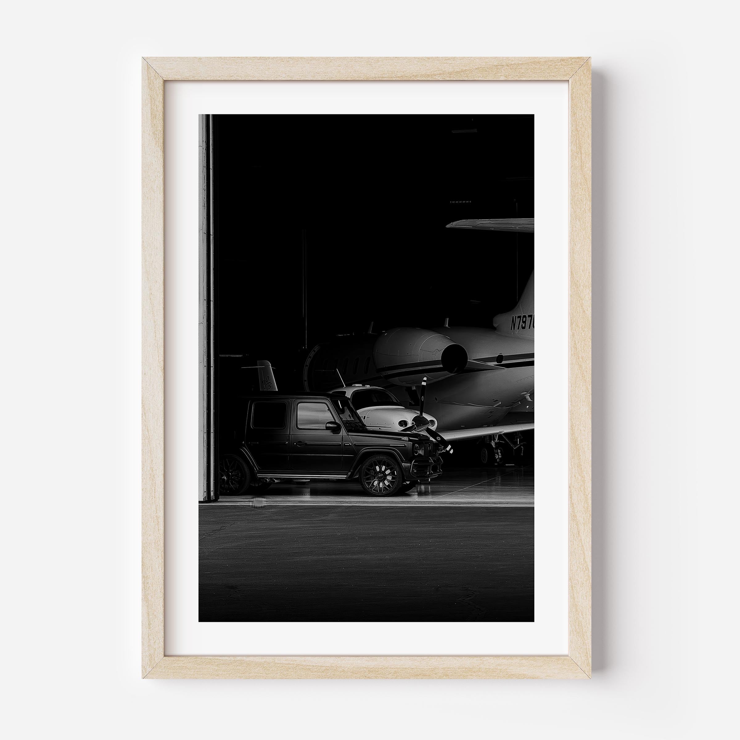 Black-and-white fine art photo of a luxury SUV parked inside an aircraft hangar with a private jet in the background.