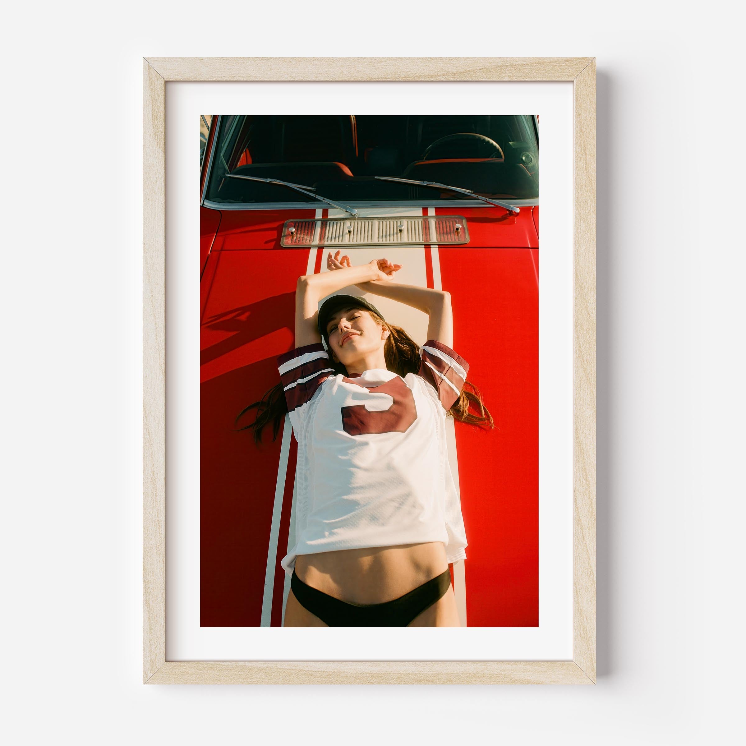 Fine art wall print of a young woman lying on a red car, evoking nostalgic teenage summer memories and carefree youth.