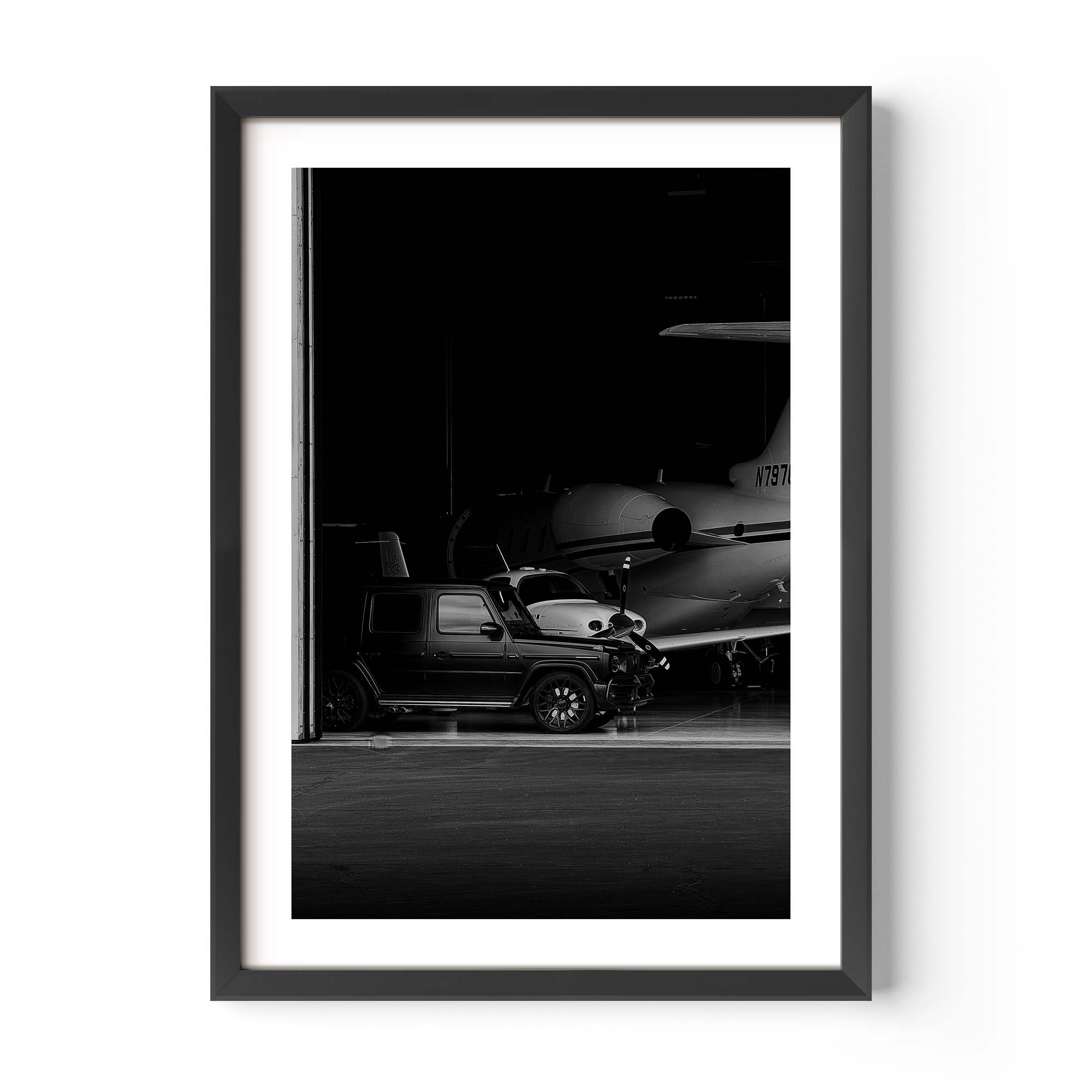 Black-and-white fine art photo of a luxury SUV parked inside an aircraft hangar with a private jet in the background.