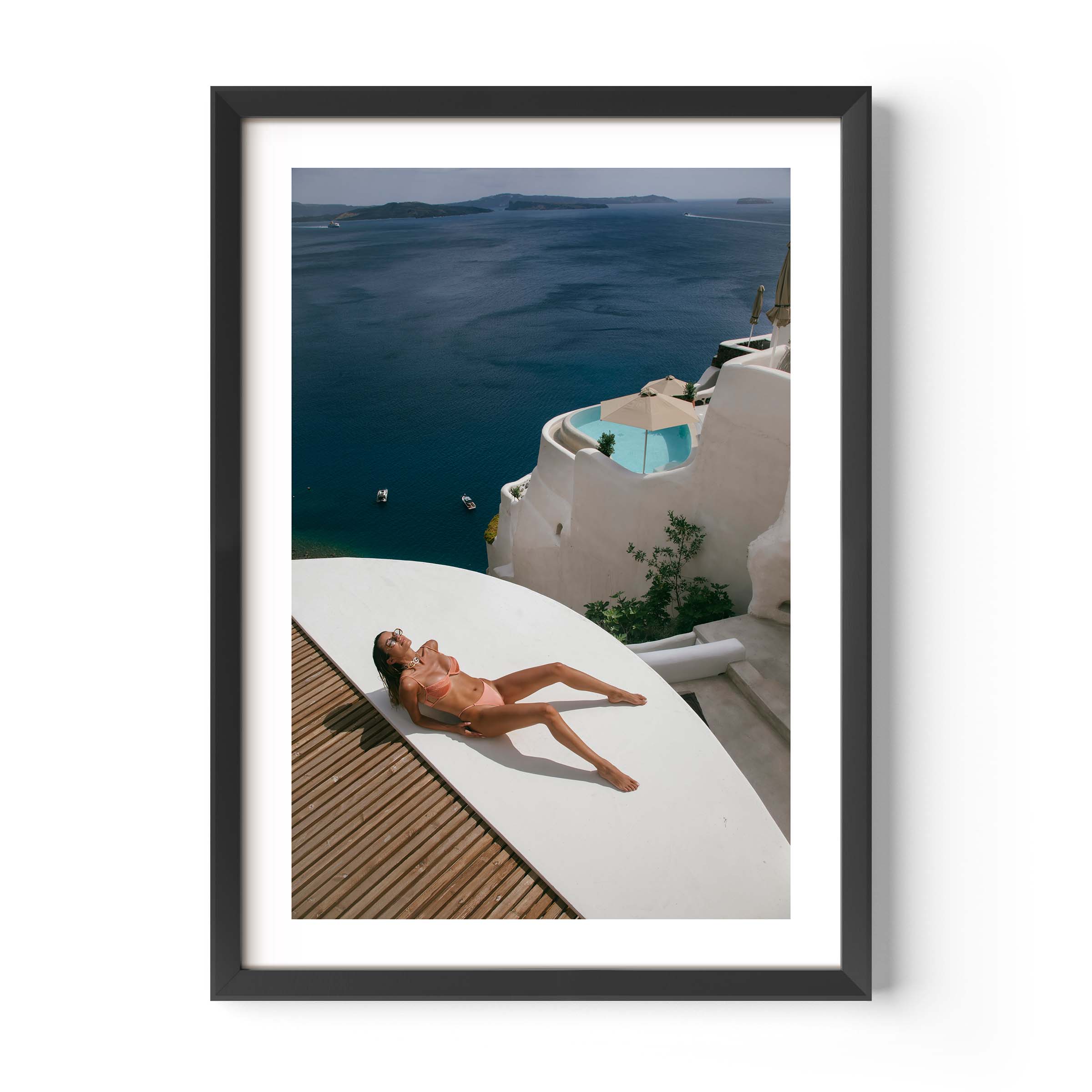 Woman sunbathing on a white terrace above a deep blue sea with whitewashed villas and a plunge pool, photographed by Britt van der Meijden