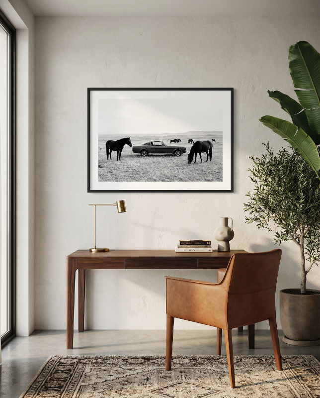 Black and white framed wall art print showing a classic car parked in a field with horses grazing in the background.