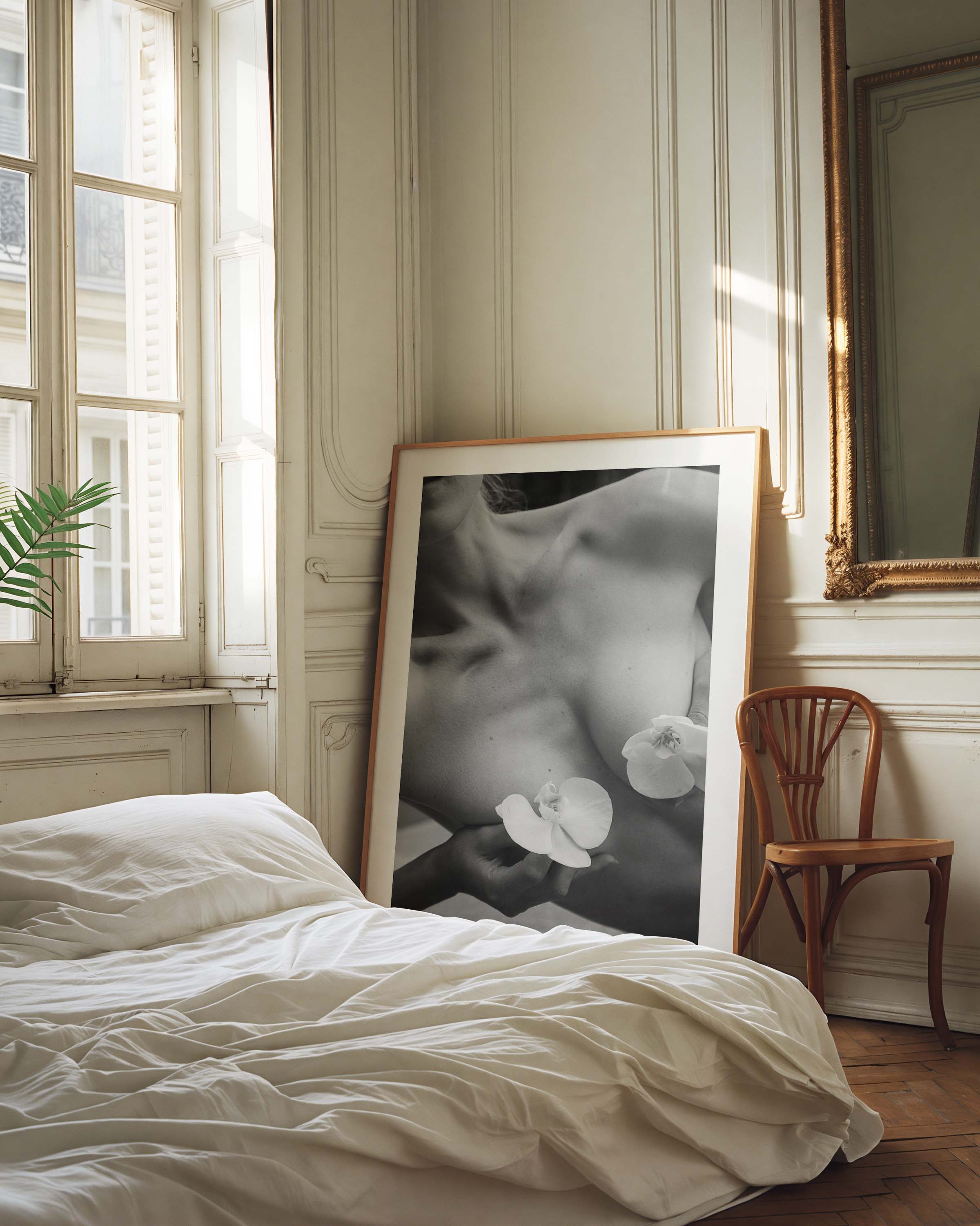 Framed black-and-white photograph of a woman’s collarbone with white orchid flowers, styled in a Parisian interior with molding, mirror, and chair — by Britt Van der Meijden.