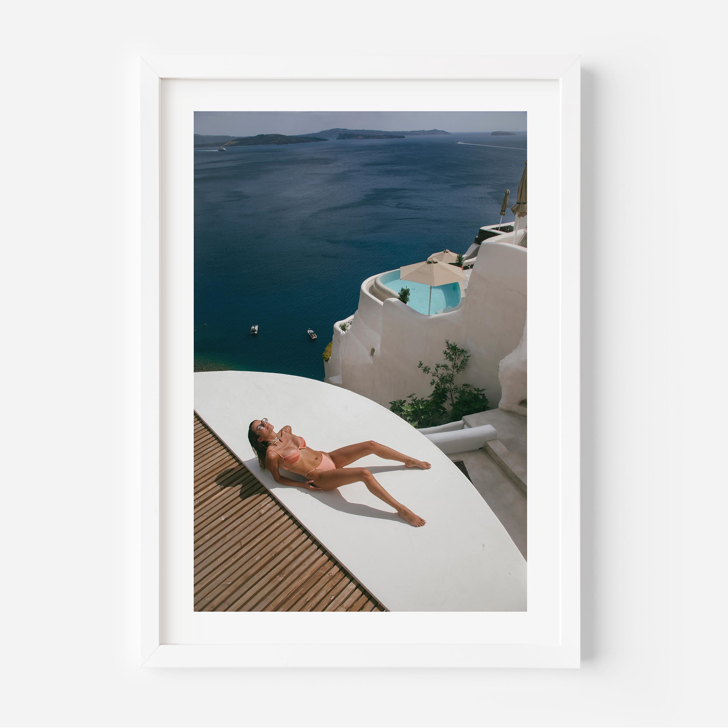 Woman sunbathing on a white terrace above a deep blue sea with whitewashed villas and a plunge pool, photographed by Britt van der Meijden