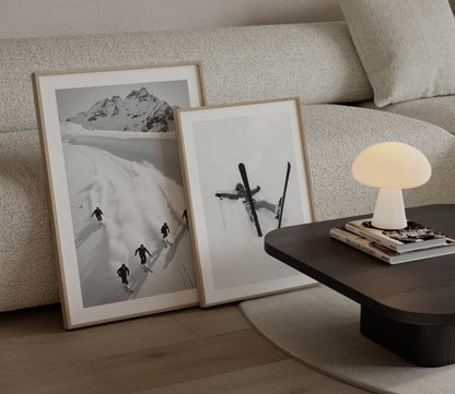 Black and white fine art print of five skiers carving through snow with mountains in the background, framed in black.