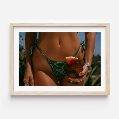 Framed fine-art photograph of a woman in an emerald snakeskin bikini holding a cocktail with a watermelon garnish; summer fashion editorial by Britt Van der Meyden.