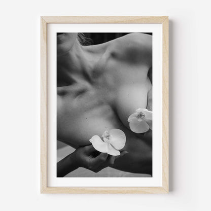 Framed black-and-white photograph of a woman’s collarbone with white orchid flowers, styled in a Parisian interior with molding, mirror, and chair — by Britt Van der Meijden.