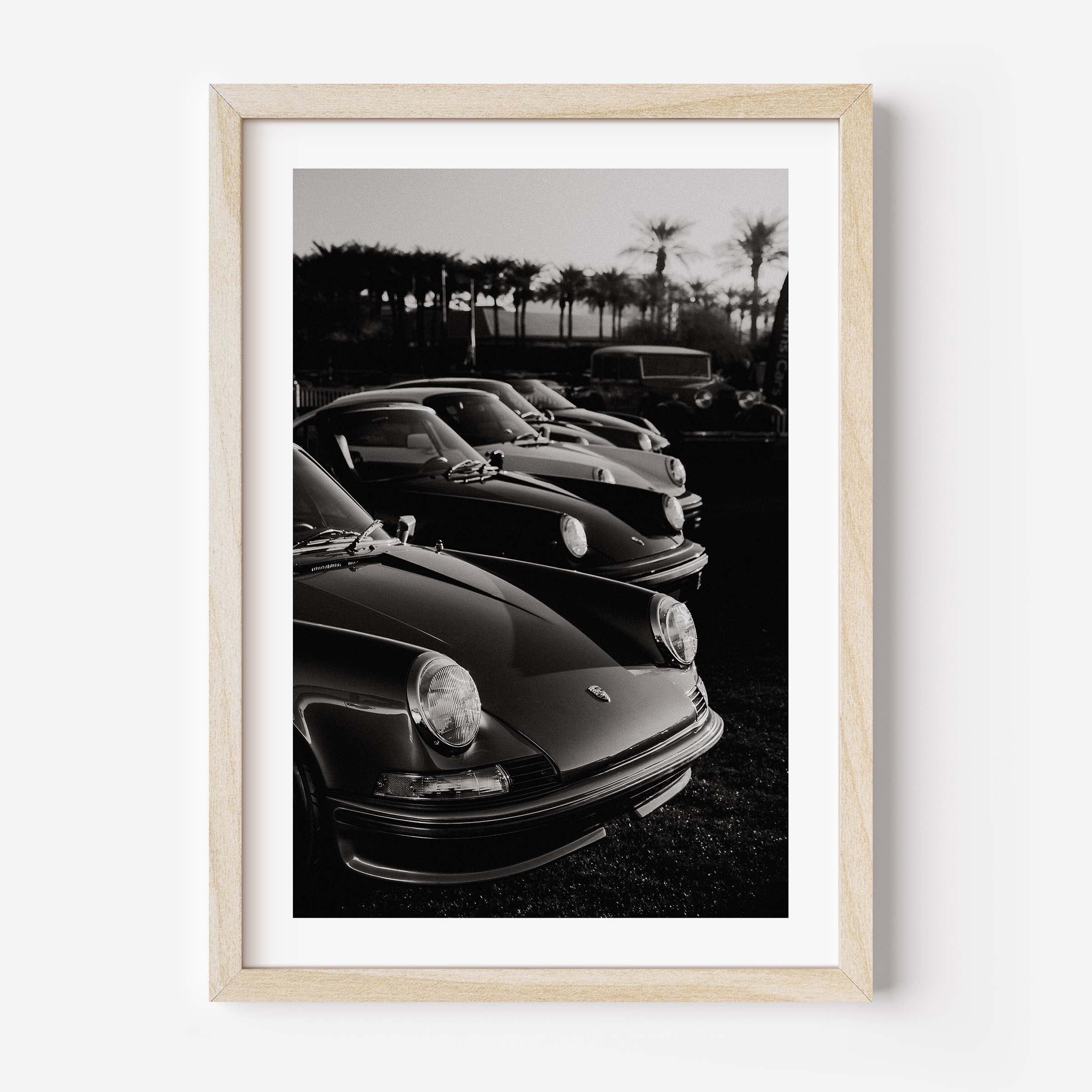 Black-and-white photo print of a row of classic Porsche 911 sports cars parked with palm trees in the background.
