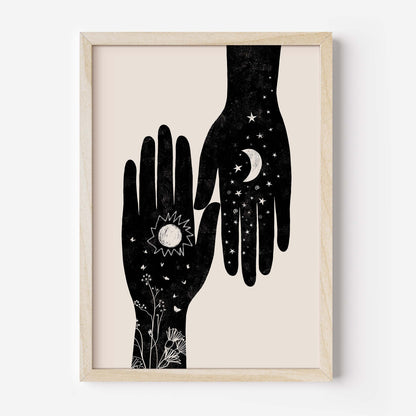 Framed wall art featuring a minimalist black illustration of two hands with celestial and floral details on a warm cream background, set in a light natural wood frame.