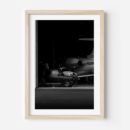 Black-and-white fine art photo of a luxury SUV parked inside an aircraft hangar with a private jet in the background.