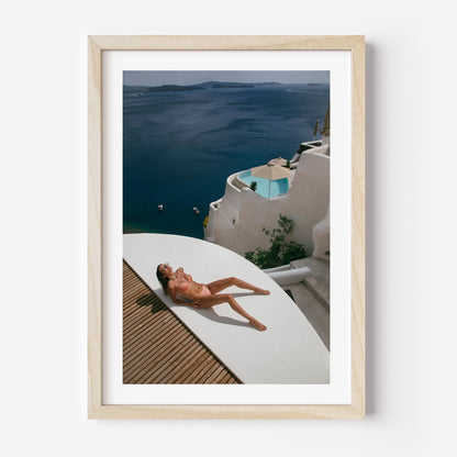 Woman sunbathing on a white terrace above a deep blue sea with whitewashed villas and a plunge pool, photographed by Britt van der Meijden