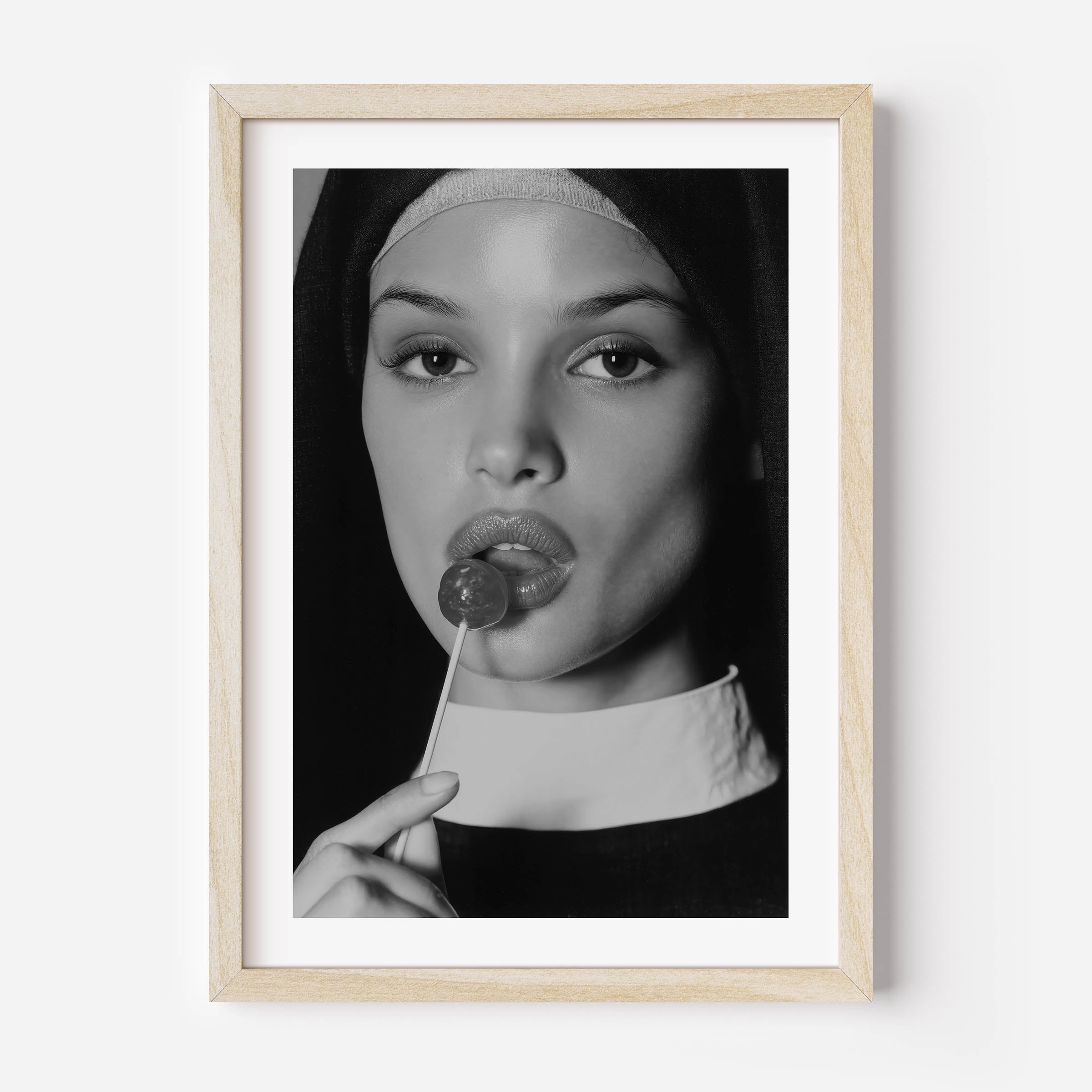 Black-and-white fine art photograph of a woman dressed as a nun, sensually holding a lollipop to her lips.