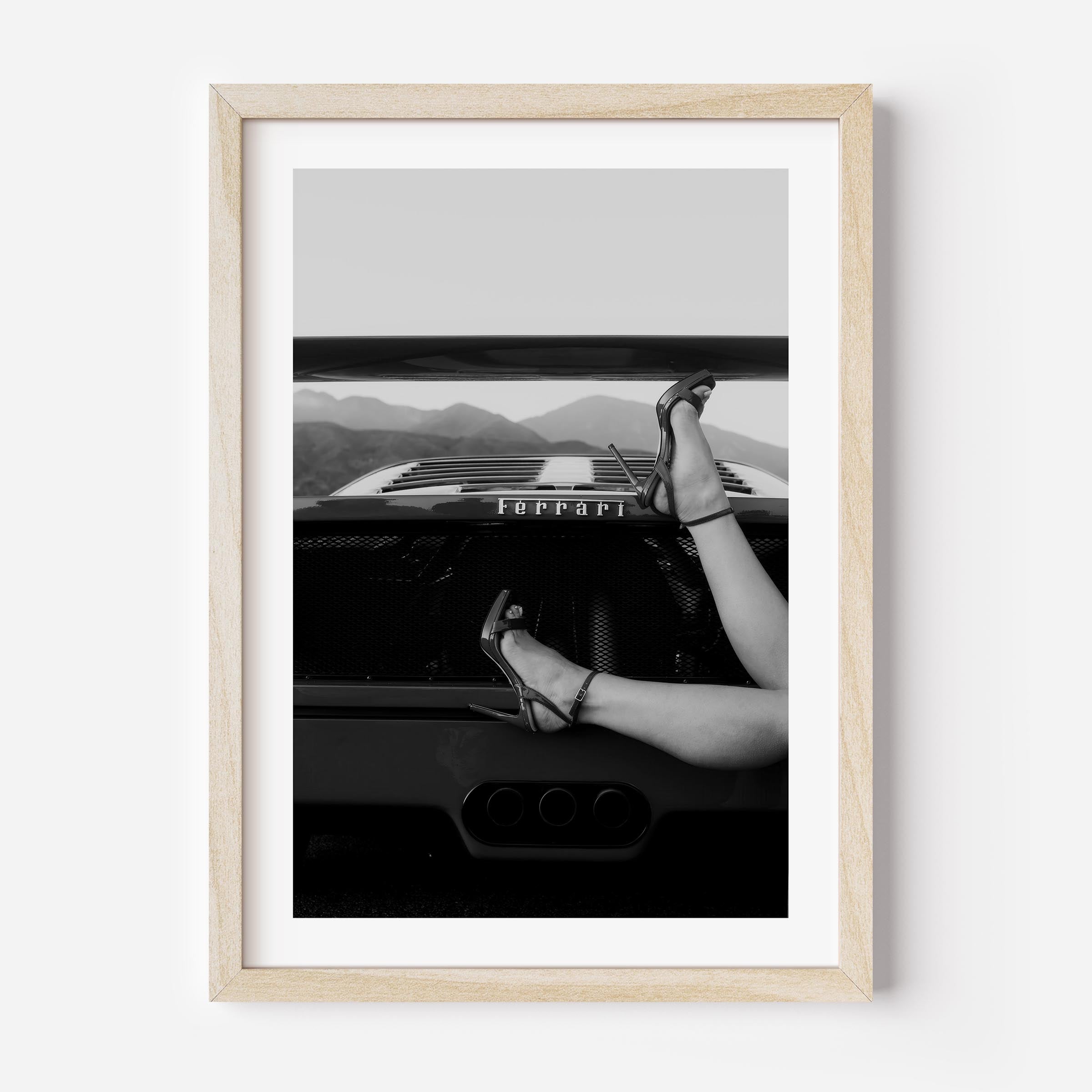Black-and-white fine art print of high heels resting on the back of a Ferrari, framed wall art.