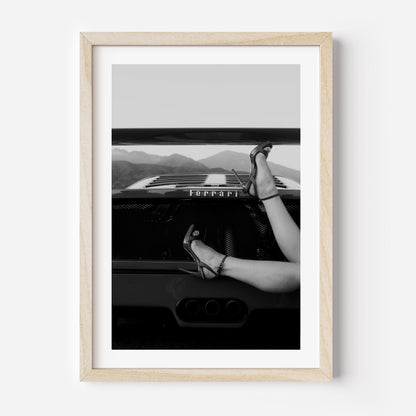 Black-and-white fine art print of high heels resting on the back of a Ferrari, framed wall art.