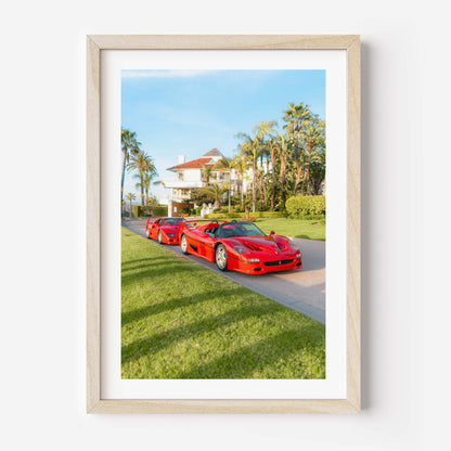 Framed fine art print of three red Italian supercars parked by a palm-lined villa on a sunny day, luxury driveway scene.