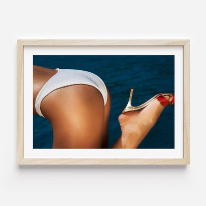 Close-up coastal photograph of a woman in a white bikini and a gold heel against deep blue water, by Britt van der Meijden