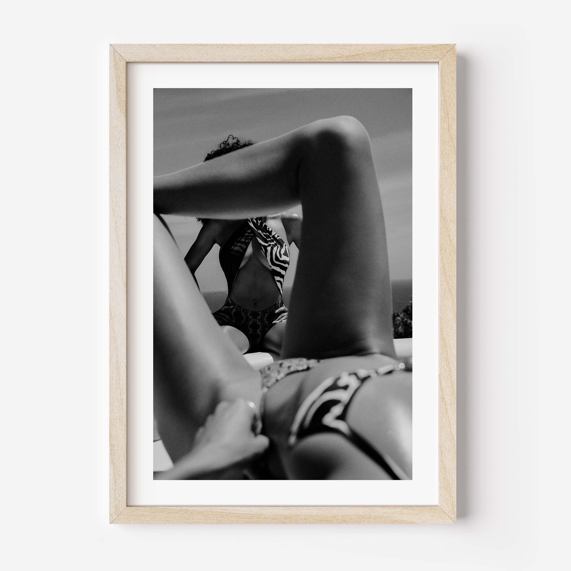 Black-and-white photo of two women relaxing poolside; foreground legs frame a seated figure in a zebra-print top, by Britt van der Meijden