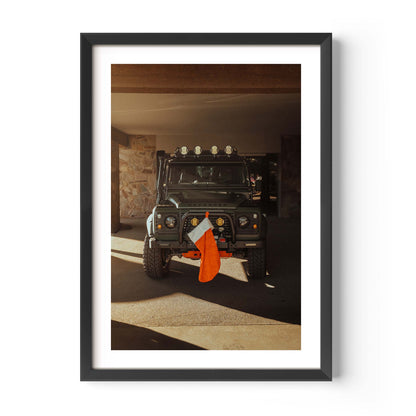 Fine art photo of a Land Rover Defender parked in a garage with warm sunlight, featuring a red Christmas stocking hanging from the front bumper.