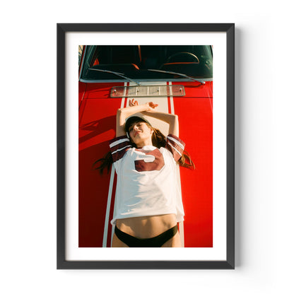 Fine art wall print of a young woman lying on a red car, evoking nostalgic teenage summer memories and carefree youth.