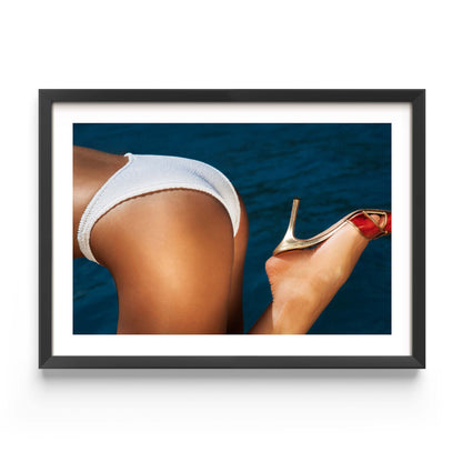Close-up coastal photograph of a woman in a white bikini and a gold heel against deep blue water, by Britt van der Meijden