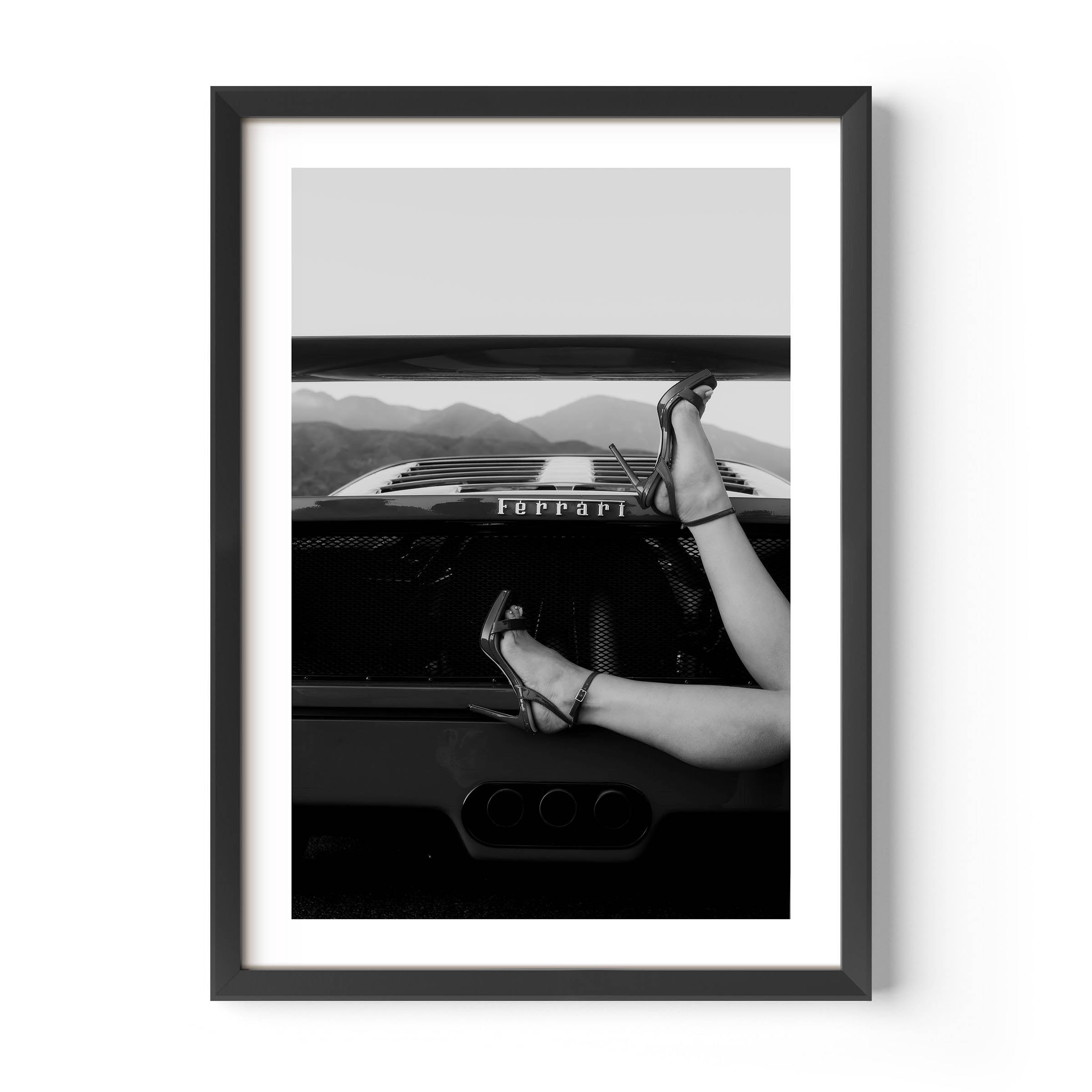 Black-and-white fine art print of high heels resting on the back of a Ferrari, framed wall art.
