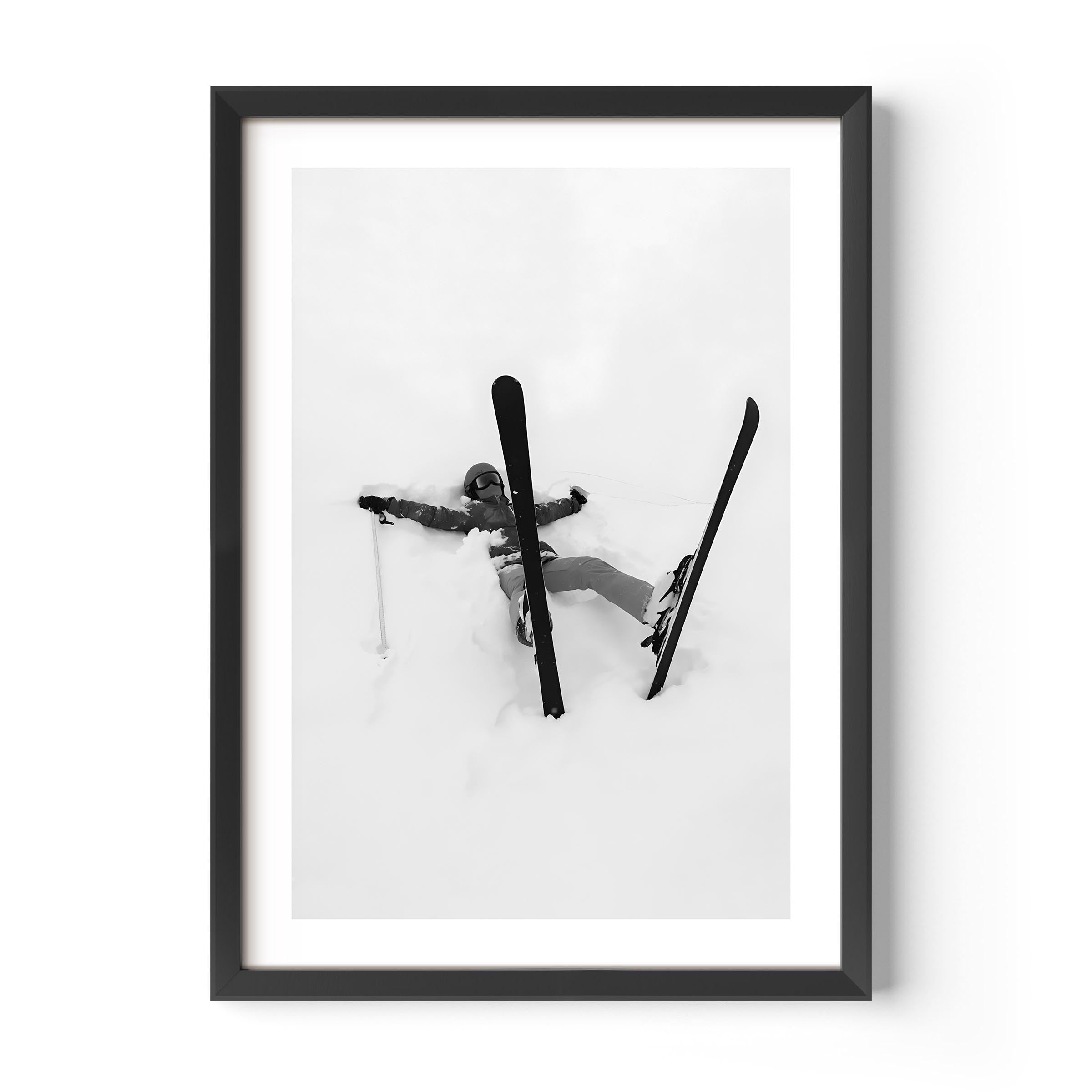 Black and white fine art print of a skier lying in deep snow with skis and pole scattered, framed in black.
