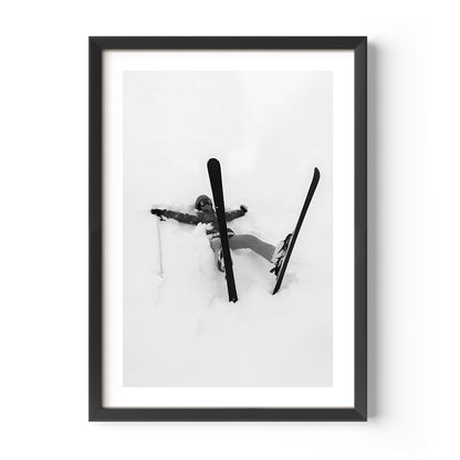 Black and white fine art print of a skier lying in deep snow with skis and pole scattered, framed in black.