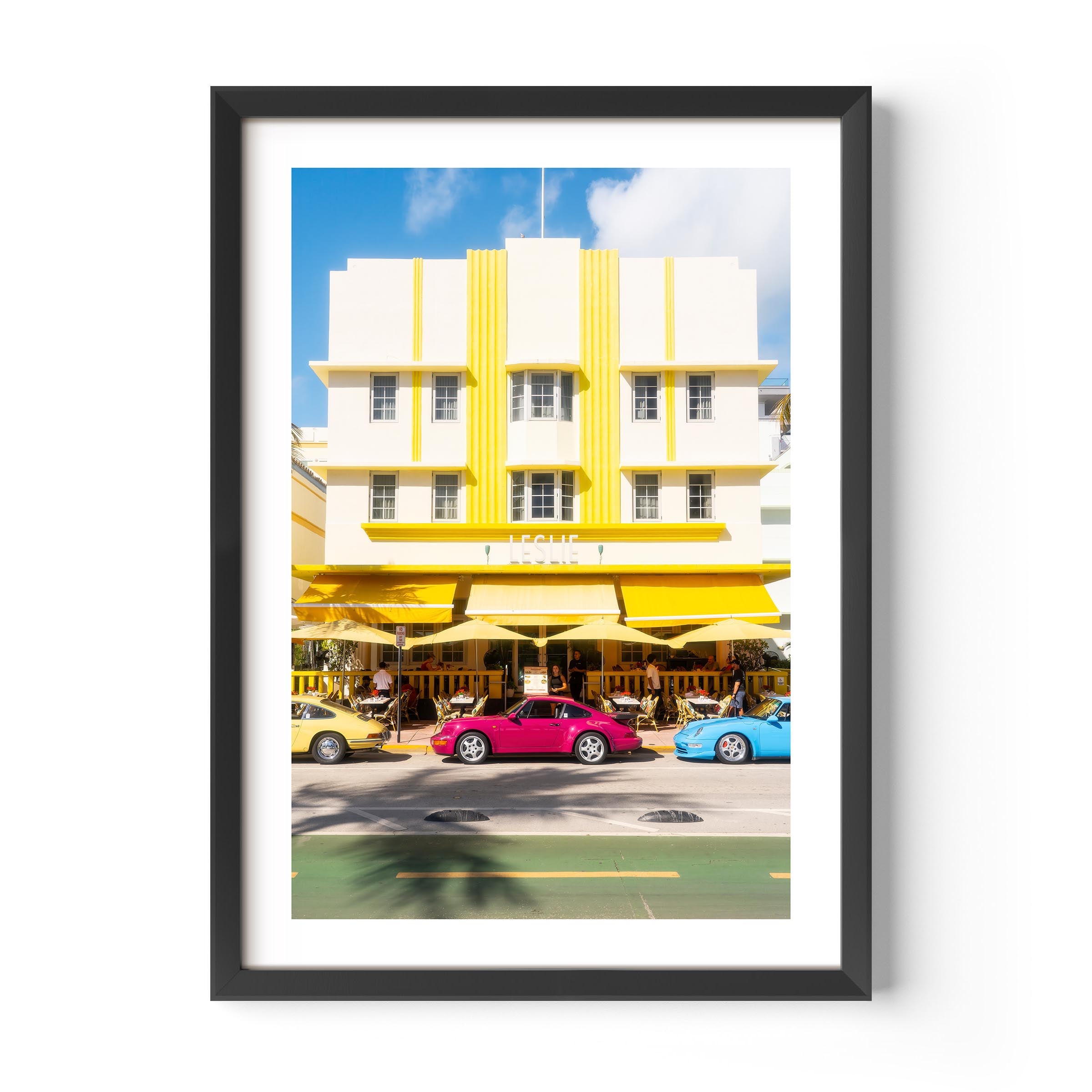 Fine art wall print of a colorful Miami street with Art Deco building and classic cars, evoking nostalgic summer road trip vibes.
