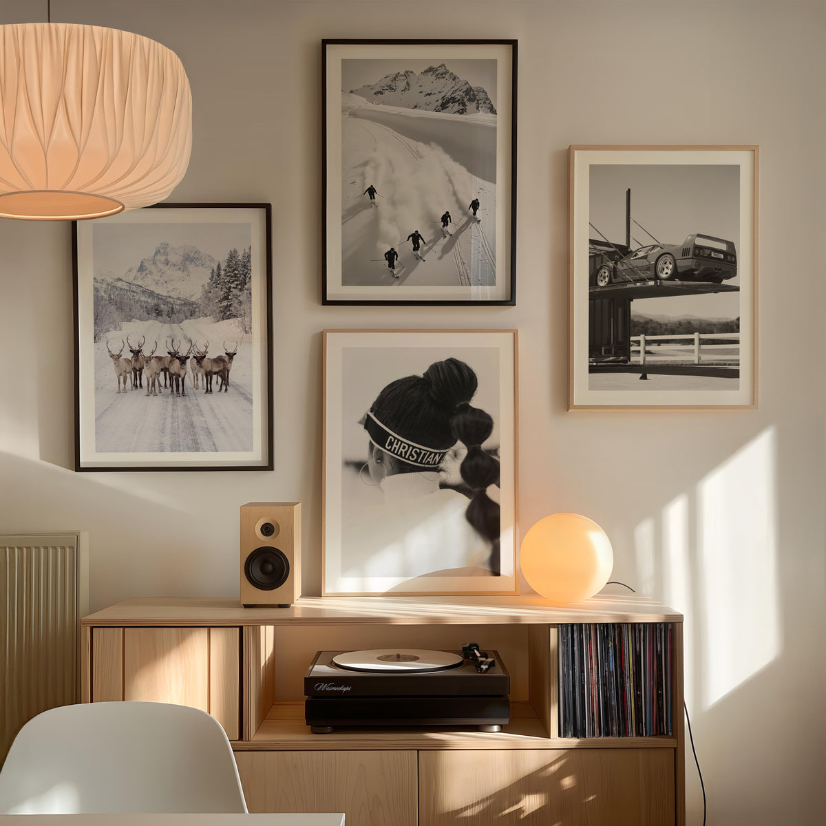 A styled interior scene showing a wall gallery of framed black-and-white and color photographs above a light wood console. The frames depict snowy mountain scenes, a skier, a car on a bridge, and a skier in action.