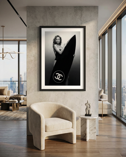Black-and-white fine art photo of a woman in a swimsuit holding a large surfboard featuring a circular double-C style logo, against a minimal studio background.