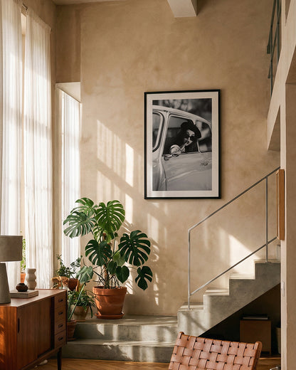 Black and white framed wall art print showing a woman in sunglasses sitting in a vintage car while applying lipstick.