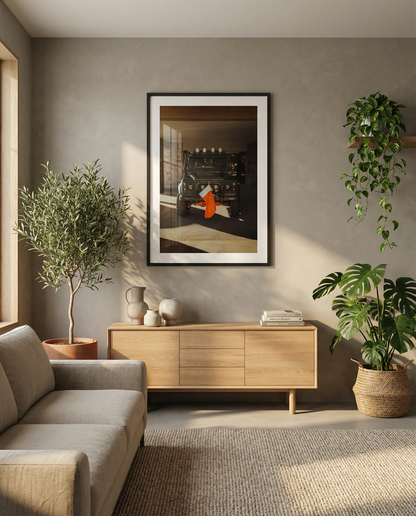 Fine art photo of a Land Rover Defender parked in a garage with warm sunlight, featuring a red Christmas stocking hanging from the front bumper.