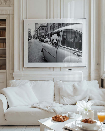 Framed black and white art print of a giant panda leaning out of a vintage classic car window on a busy city street, with urban buildings in the background. White mat border in a black frame, printed on premium 230g matte paper.