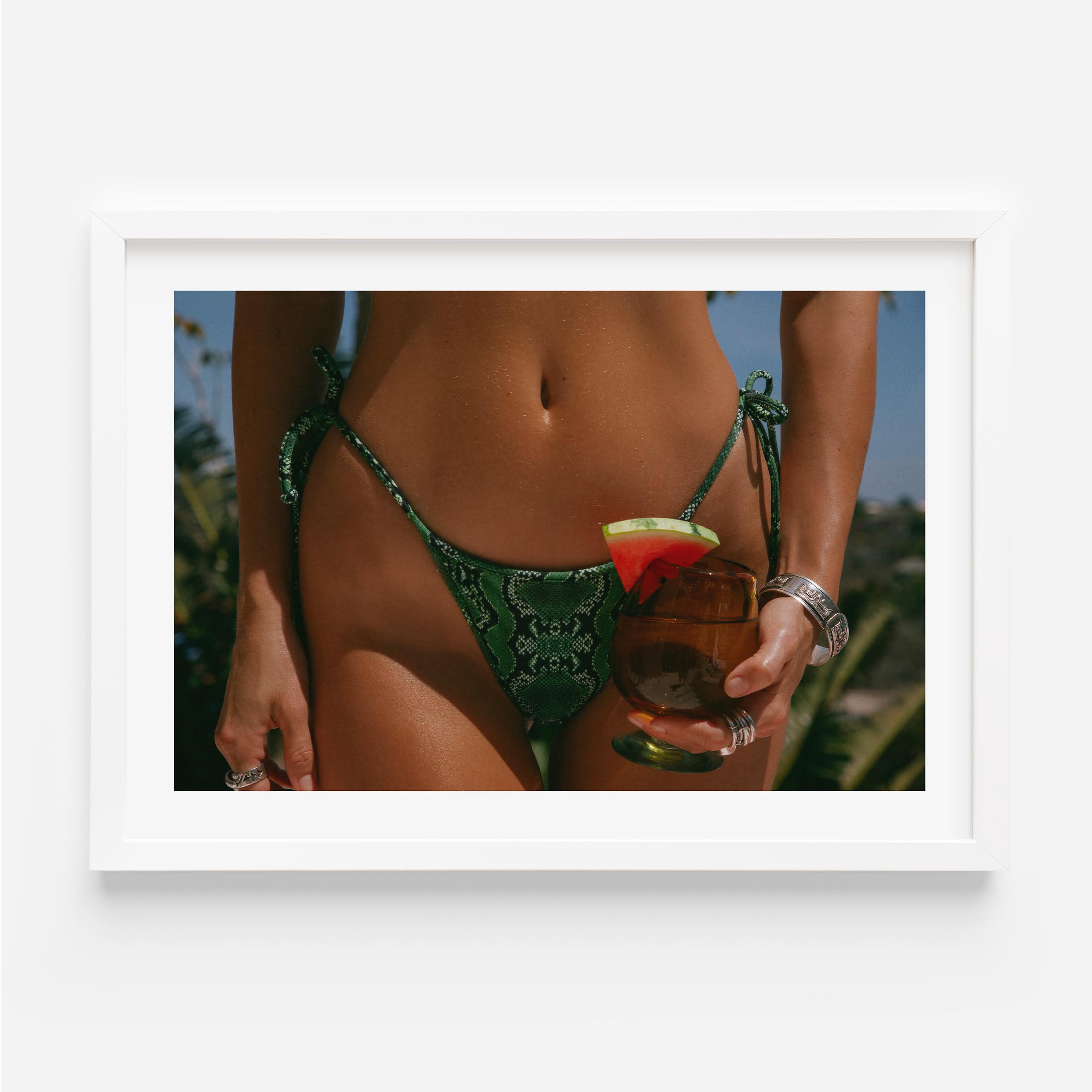 Framed fine-art photograph of a woman in an emerald snakeskin bikini holding a cocktail with a watermelon garnish; summer fashion editorial by Britt Van der Meyden.