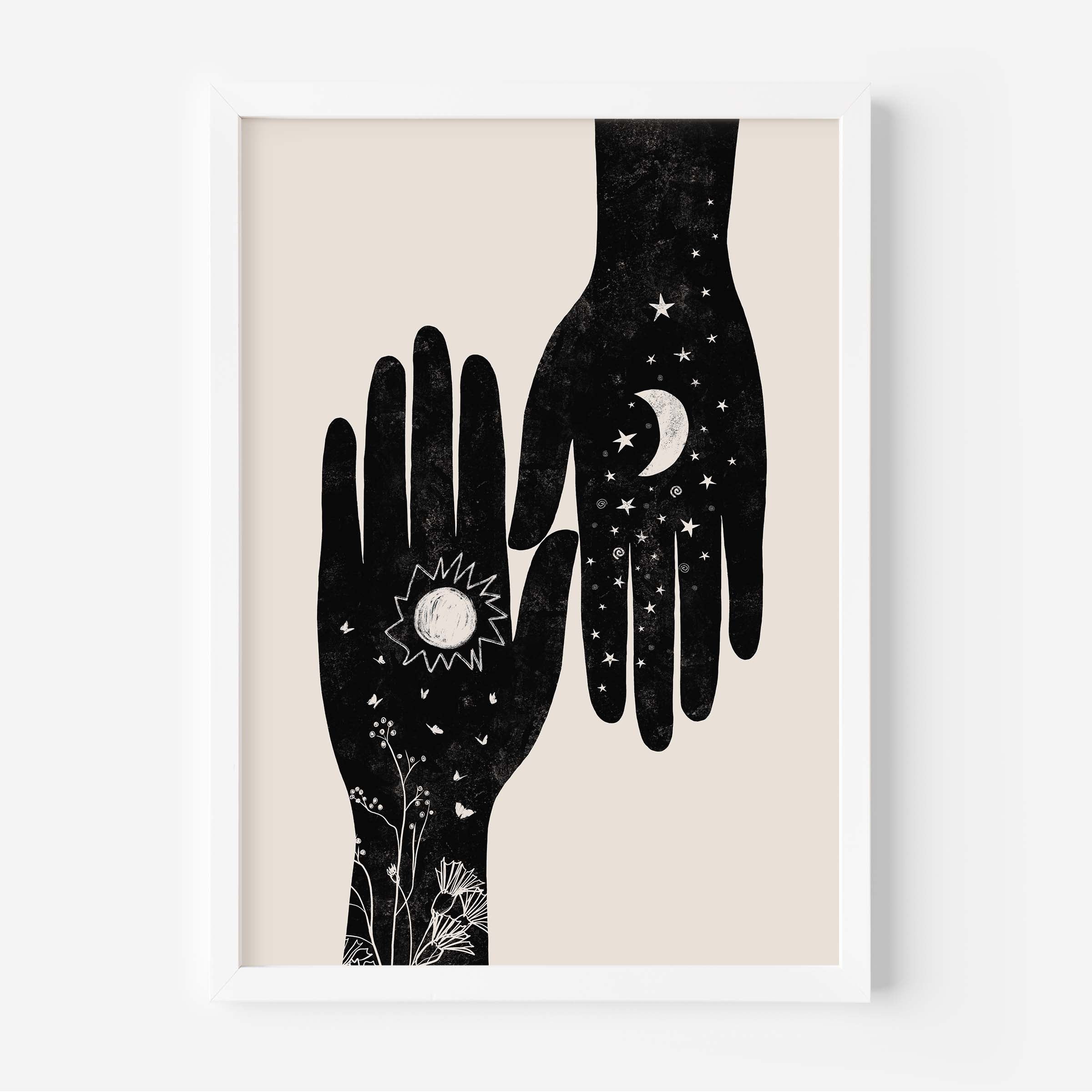 A framed art print featuring two black hands with celestial and botanical illustrations on a warm beige background, enclosed in a white frame.
