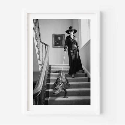 A framed black and white art print depicting a woman in a long coat and wide-brimmed hat walking a large alligator down a grand staircase, shown against a clean white background.