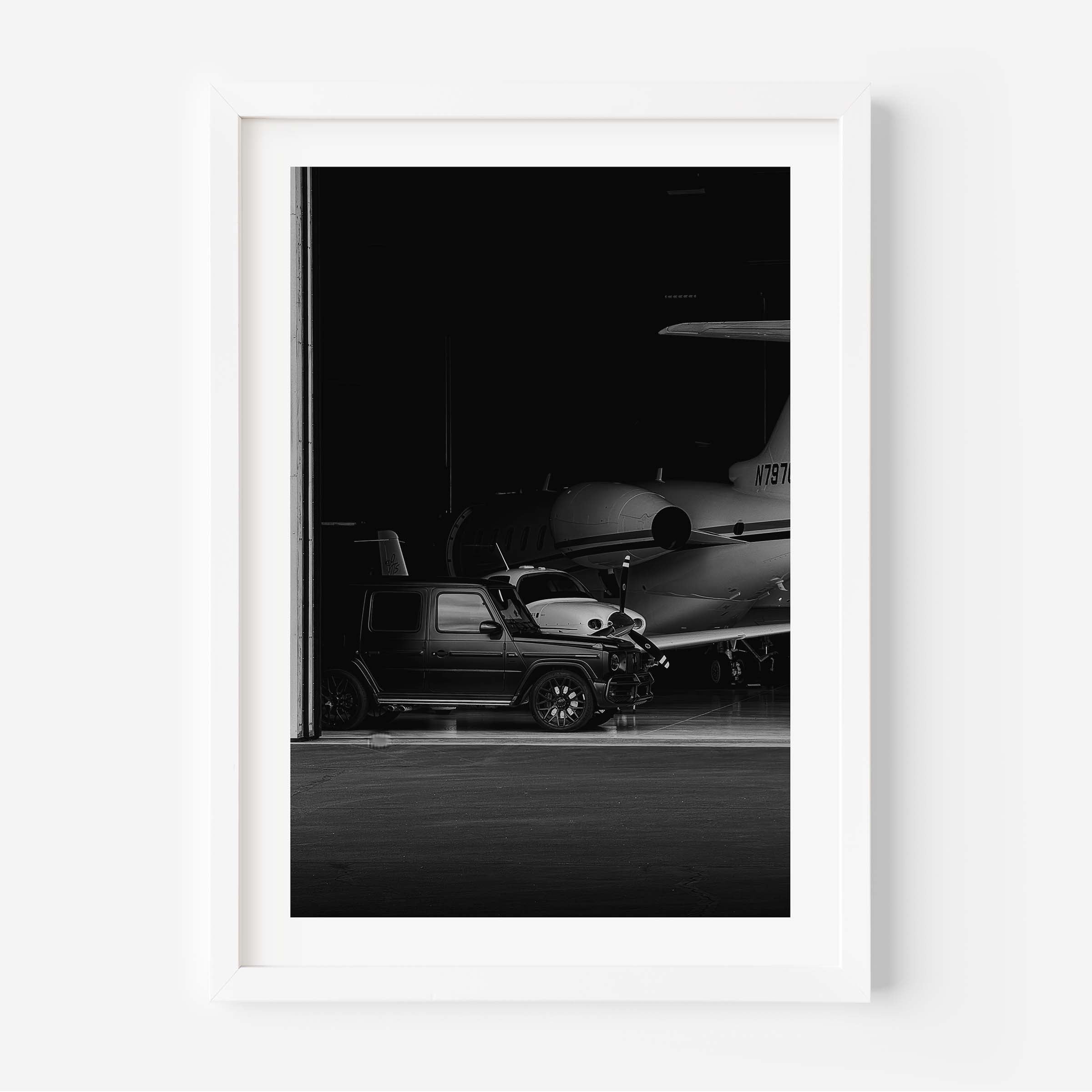 Black-and-white fine art photo of a luxury SUV parked inside an aircraft hangar with a private jet in the background.