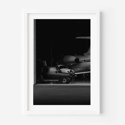 Black-and-white fine art photo of a luxury SUV parked inside an aircraft hangar with a private jet in the background.