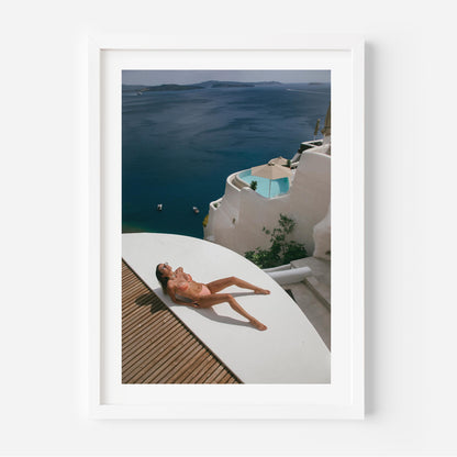 Woman sunbathing on a white terrace above a deep blue sea with whitewashed villas and a plunge pool, photographed by Britt van der Meijden