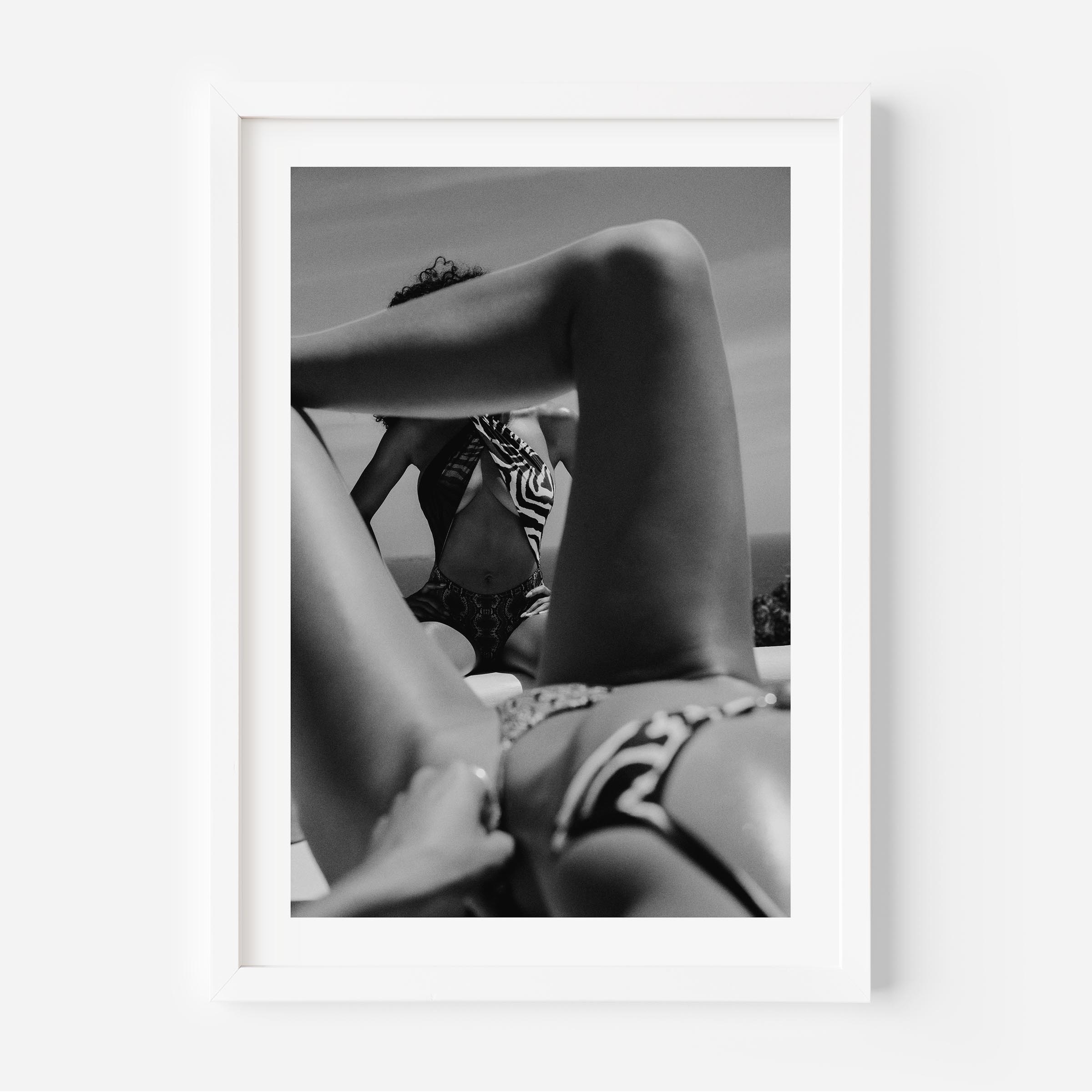 Black-and-white photo of two women relaxing poolside; foreground legs frame a seated figure in a zebra-print top, by Britt van der Meijden