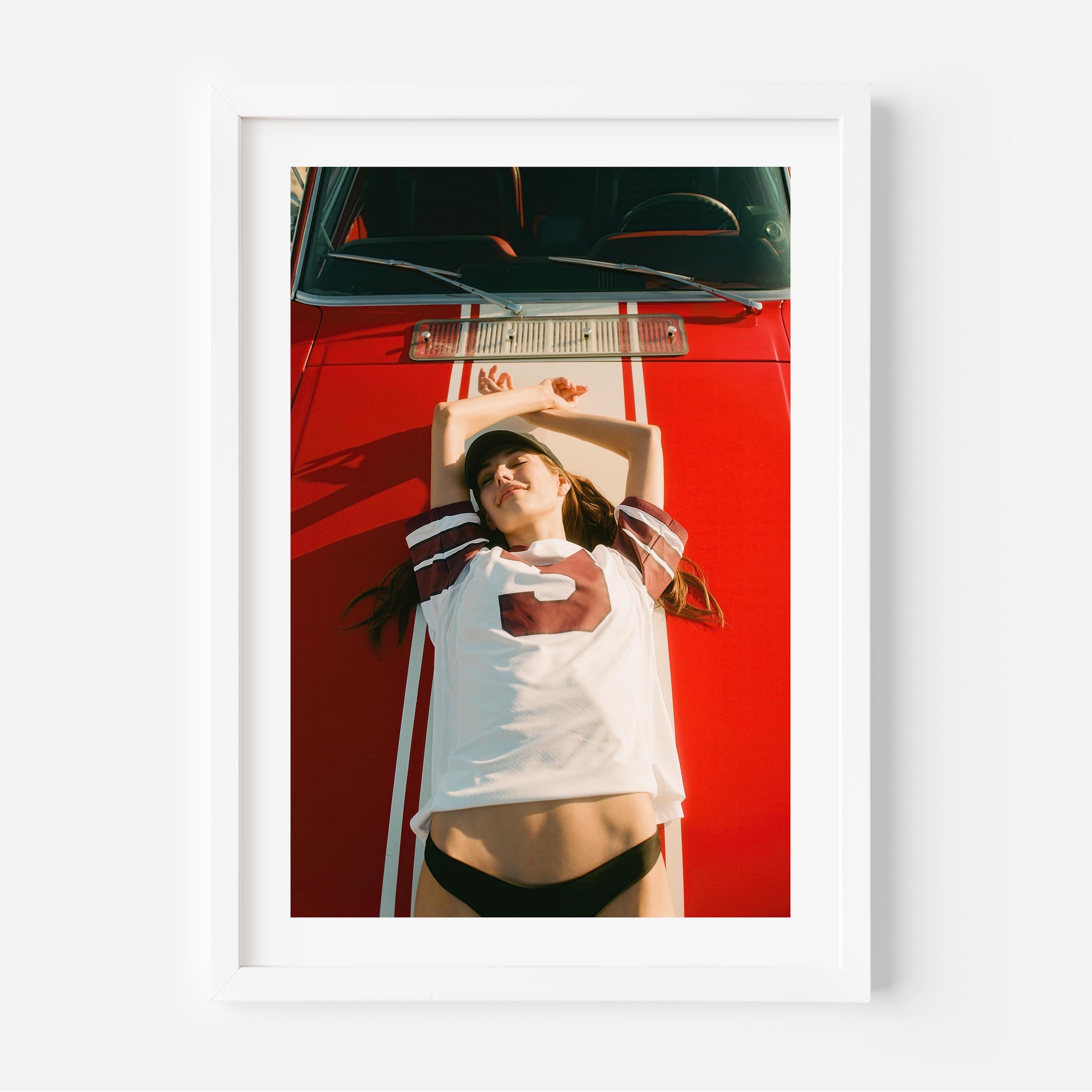 Fine art wall print of a young woman lying on a red car, evoking nostalgic teenage summer memories and carefree youth.