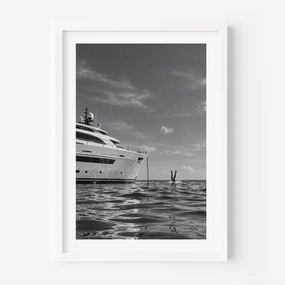 A framed black and white art print depicting a luxury yacht on the ocean, with a person standing in the water nearby, shown against a clean white background.