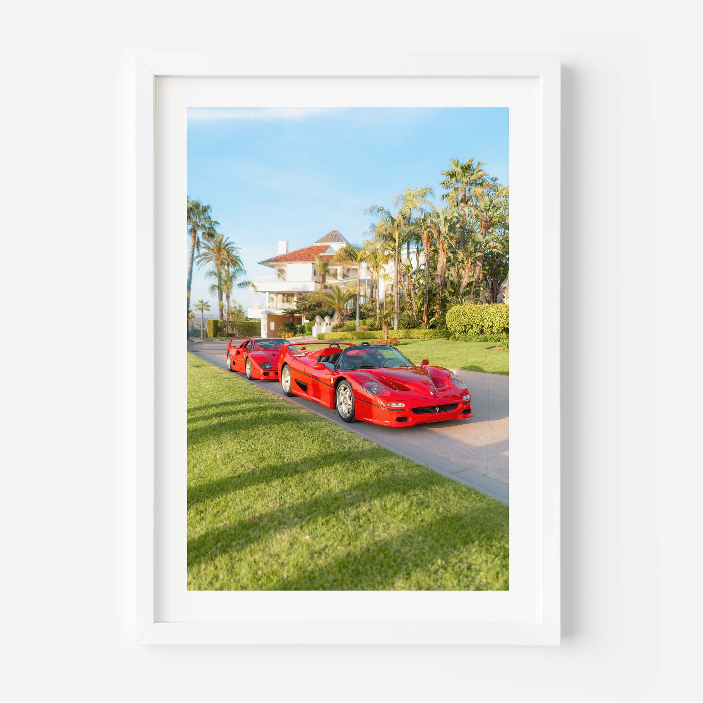 Framed fine art print of three red Italian supercars parked by a palm-lined villa on a sunny day, luxury driveway scene.