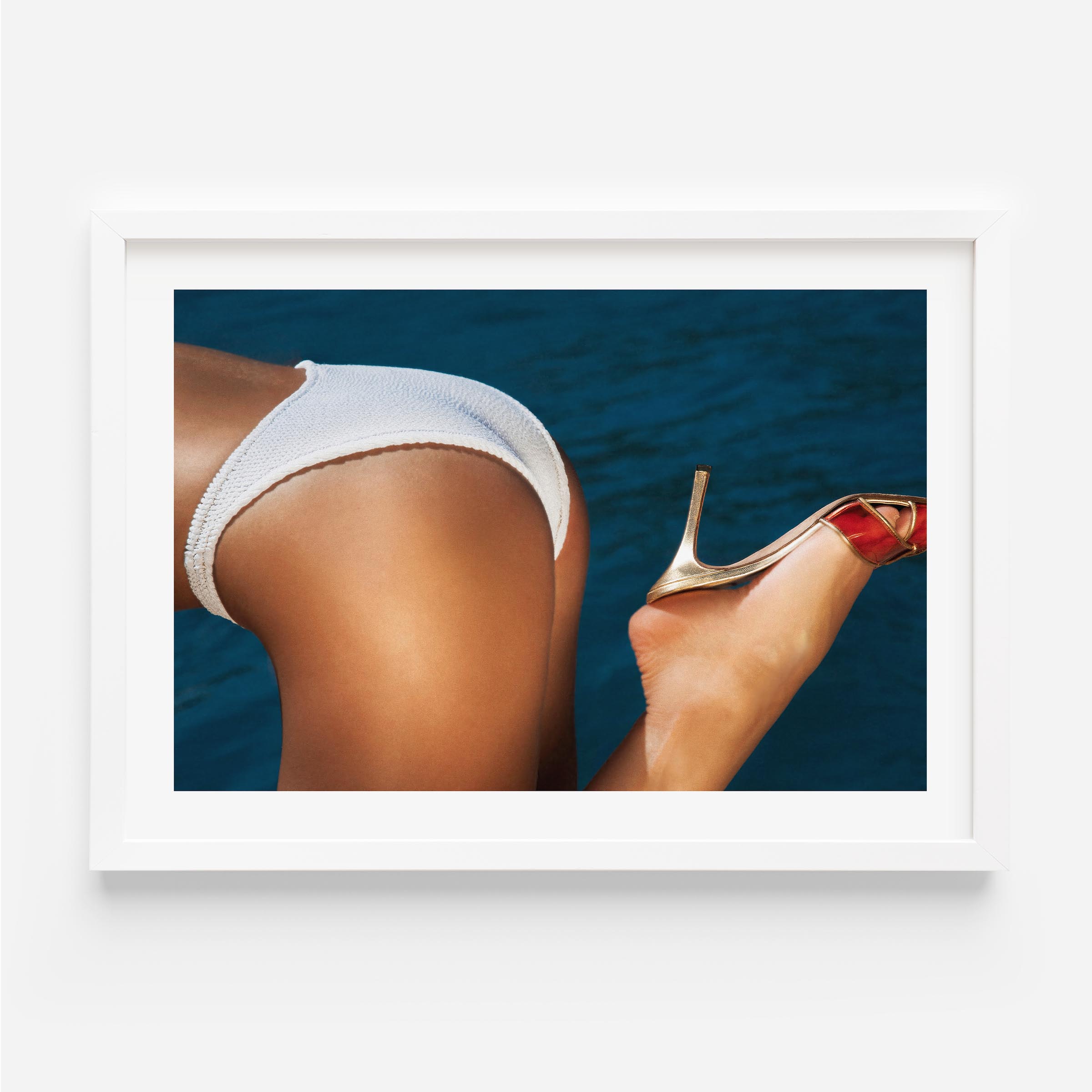 Close-up coastal photograph of a woman in a white bikini and a gold heel against deep blue water, by Britt van der Meijden