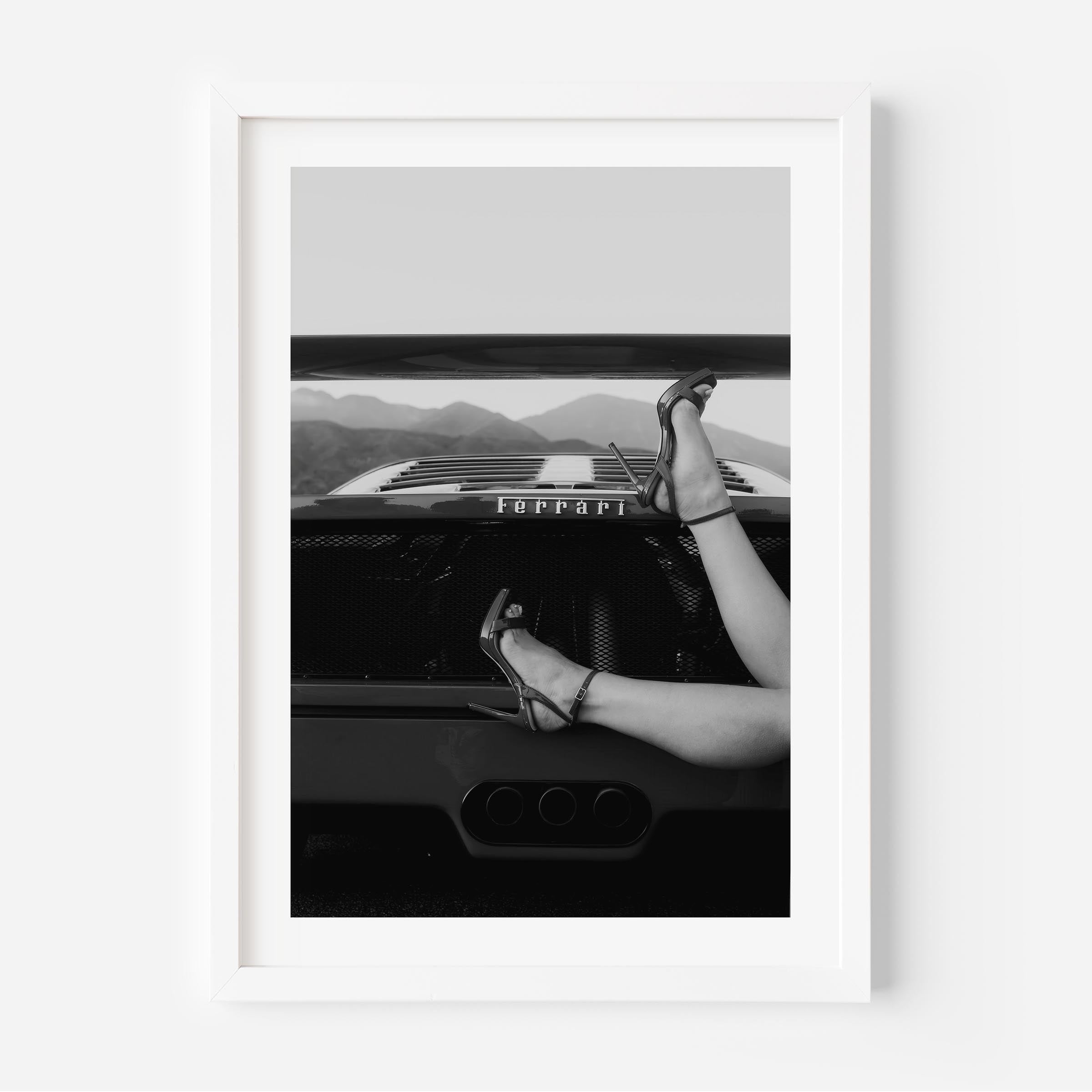 Black-and-white fine art print of high heels resting on the back of a Ferrari, framed wall art.