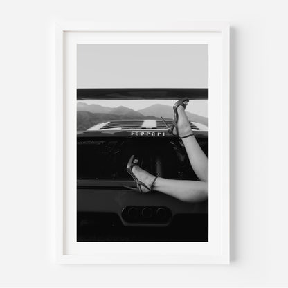 Black-and-white fine art print of high heels resting on the back of a Ferrari, framed wall art.