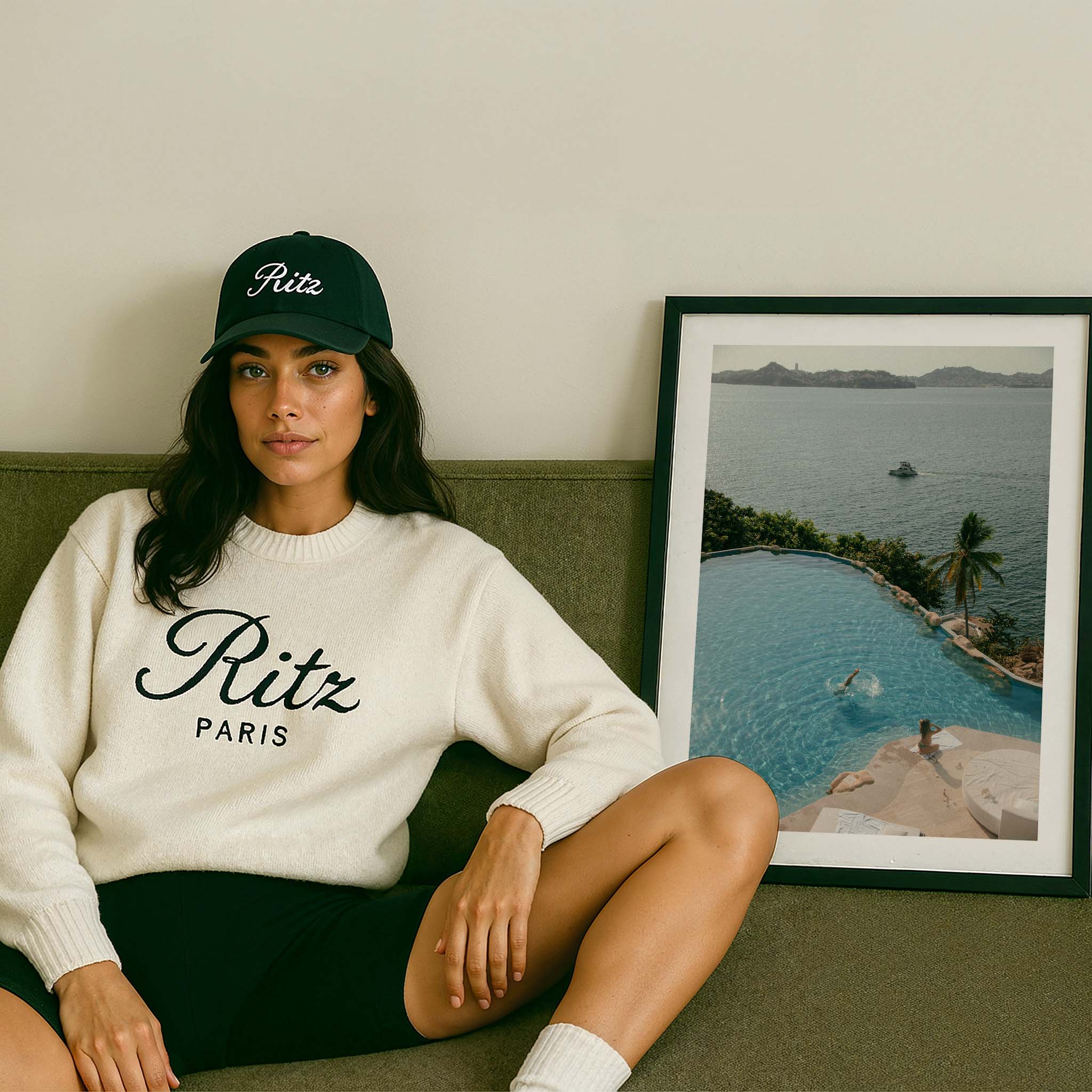Framed color photograph of a diver in a turquoise infinity pool above a tropical bay with palm tree, sunlounger and boat in the distance — by Britt Van der Meyden.