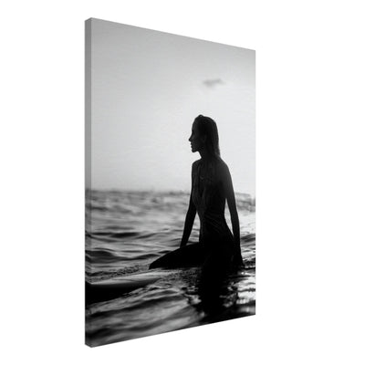 black and white canvas print of a woman sitting on a surfboard in the ocean during sunset